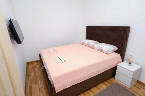 Spavaća soba sa bračnim krevetom, noćnim stočićem i televizorom na zidu. - image 4