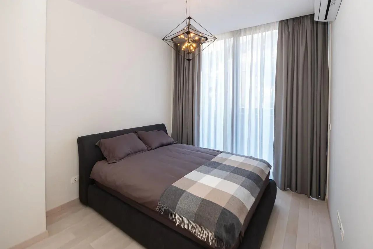 Moderna spavaća soba sa bračnim krevetom, zavjesama i lusterom.