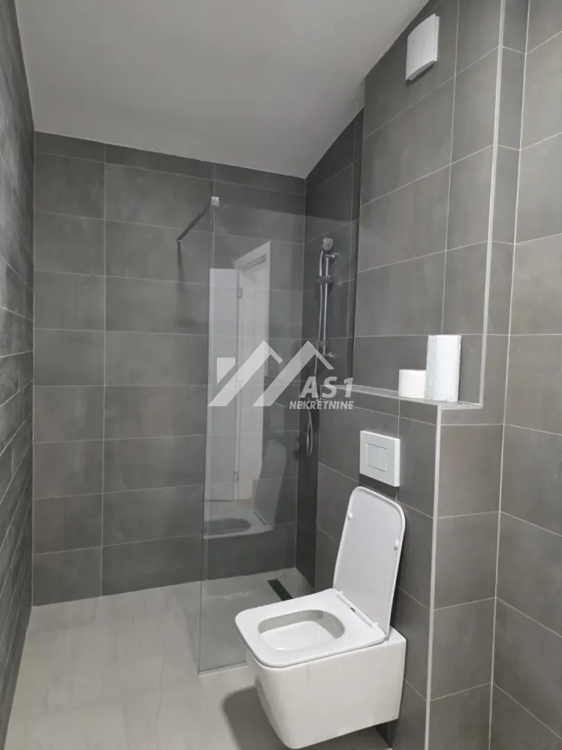 Moderno opremljeno kupatilo sa tuš kabinom i wc šoljom obloženo sivim pločicama.