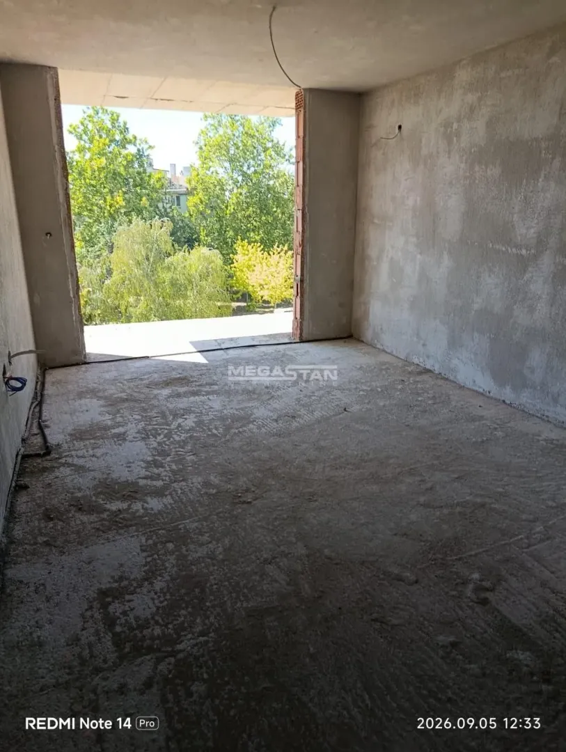 Unfinished room in grey phase of construction with a view of greenery.