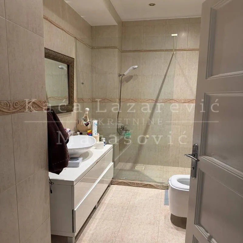 Kupatilo sa tuš kabinom, umivaonikom i WC šoljom obloženo keramičkim pločicama.