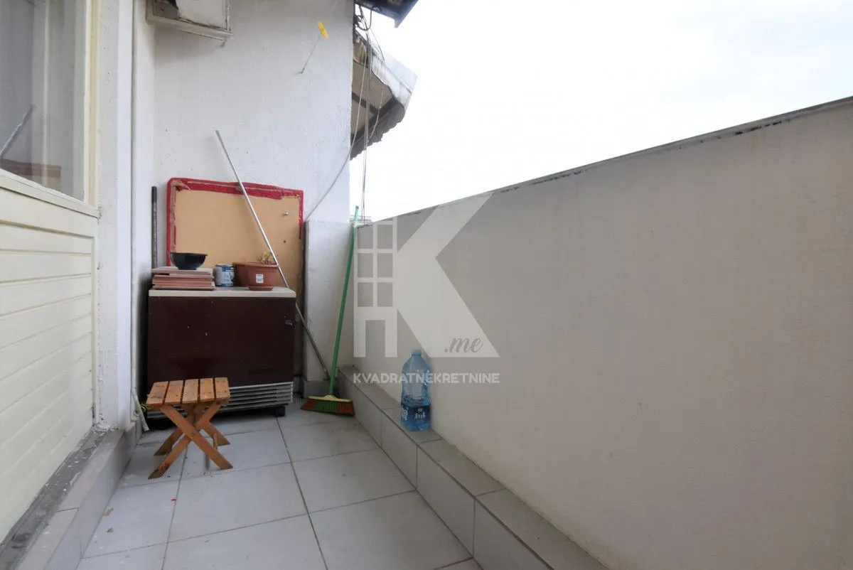 Manji popločani balkon sa ormarićem i drvenom stolicom.
