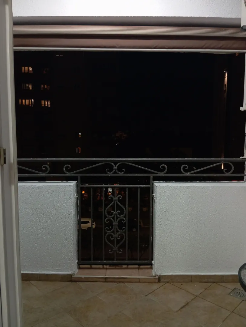 Natkriveni balkon sa metalnom ogradom i pogledom noću.