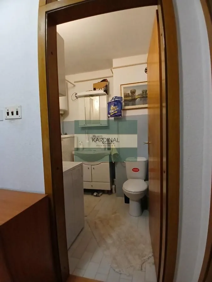 Pogled iz hodnika na kupatilo sa umivaonikom, WC šoljom i veš mašinom.
