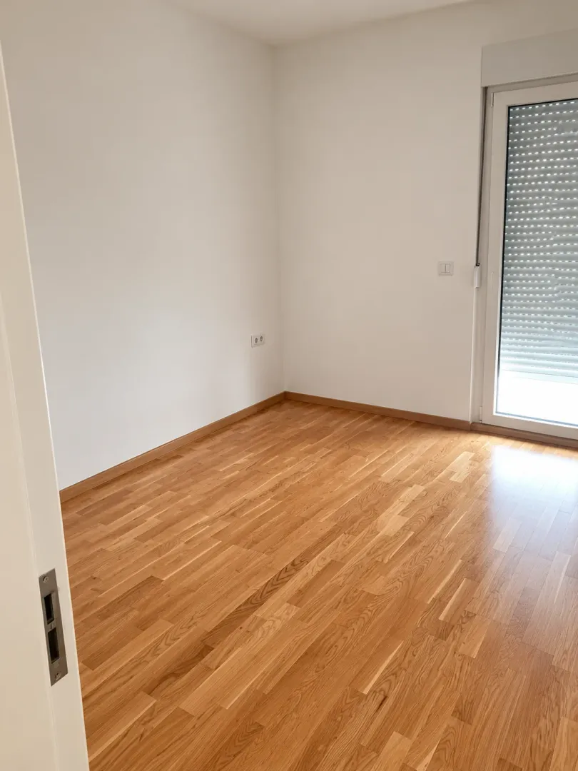 Prazna soba sa parketom i balkonskim vratima.