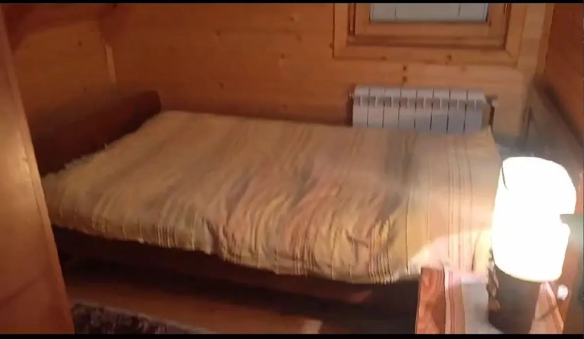 Spavaća soba sa drvenim zidovima i svijetlim prekrivačem na krevetu.