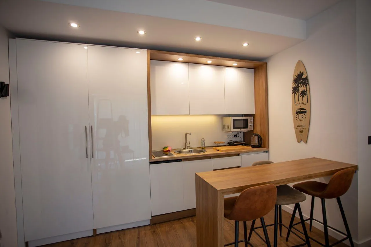 Modern kitchen with white cabinetry, wooden details, and a breakfast bar with stools.