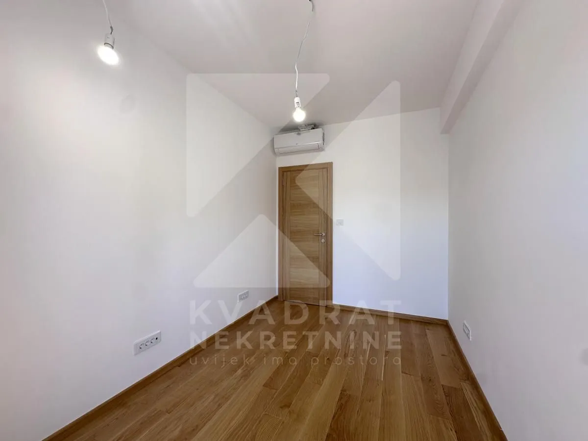 Empty room with wooden flooring, white walls, and an air conditioning unit.