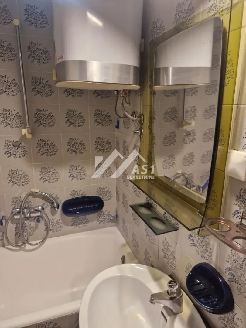 Small bathroom with a bathtub, washbasin, mirror, and water heater.