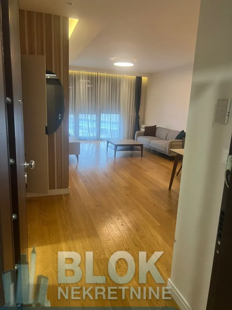 View from the hallway into a furnished living room with hardwood floors and large windows.