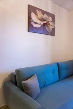 Comfortable blue sofa against a white wall with a floral painting. - image 7