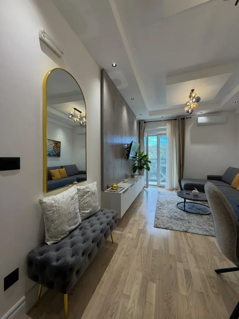 Modern and bright living room with a sofa, TV console, and a large mirror.