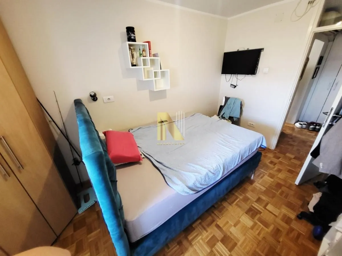 Nameštena spavaća soba sa bračnim krevetom, ormarom i zidnim televizorom.