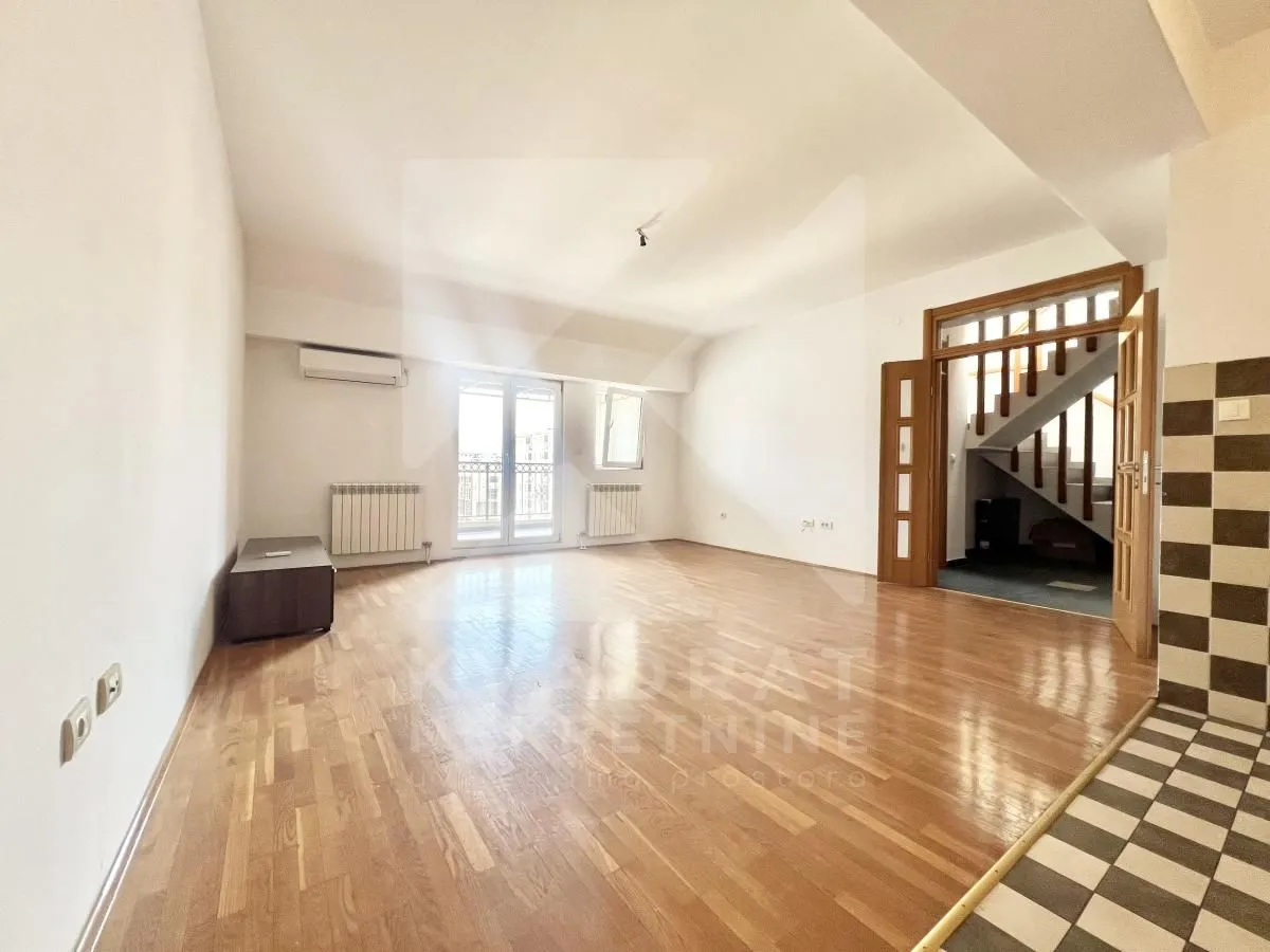Spacious empty living room with wooden flooring and a staircase in the background.