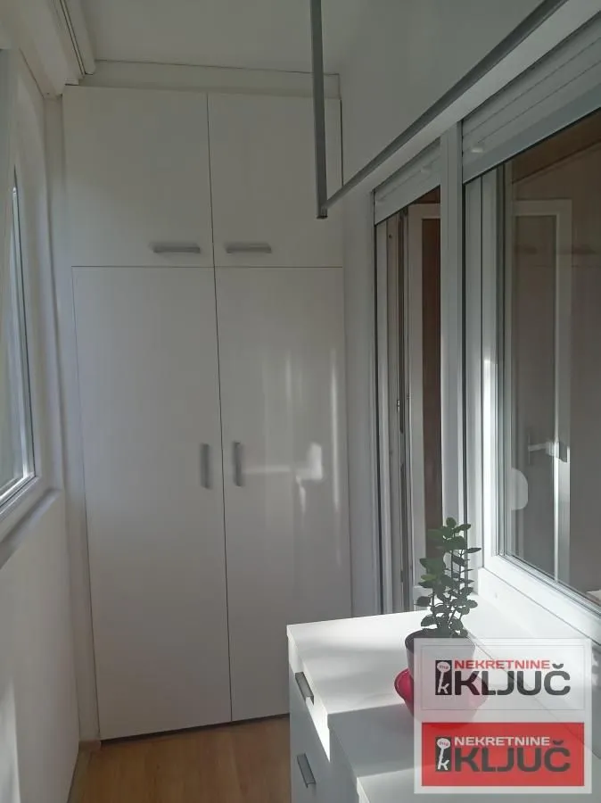 Zastakljena terasa sa ugradnim ormarom i stolom sa saksijom cveća.