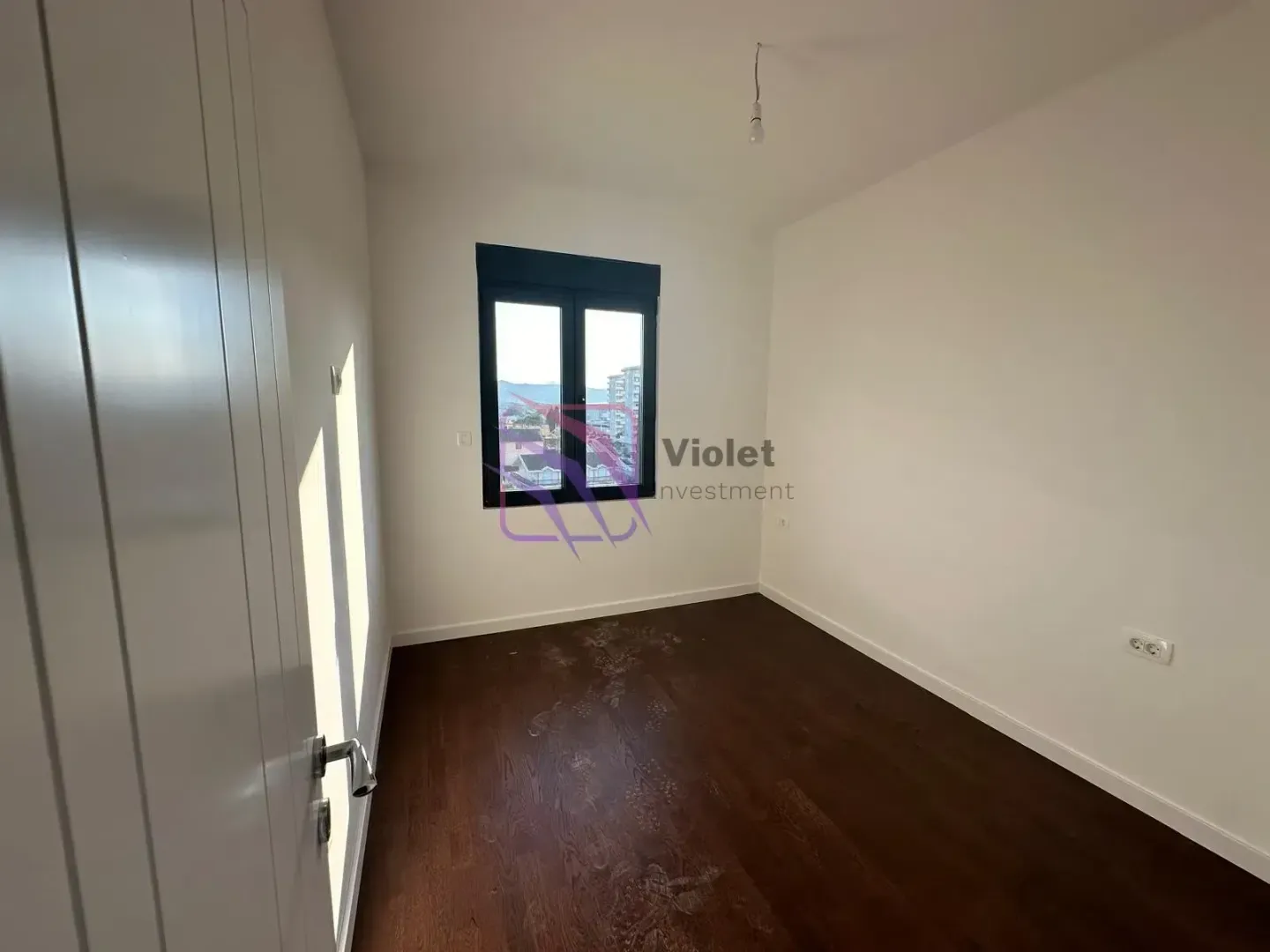 Empty room with dark wooden flooring and a window overlooking the city.