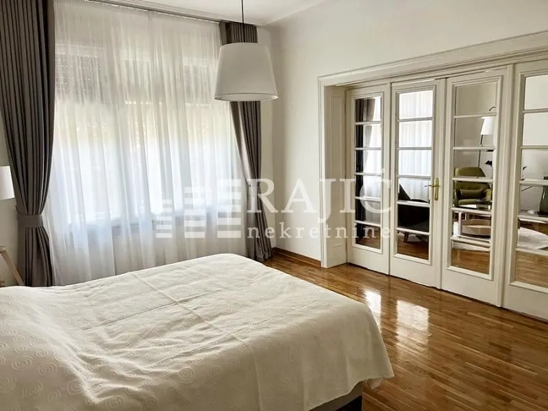 Spacious bedroom with a double bed, hardwood floors, and large windows.