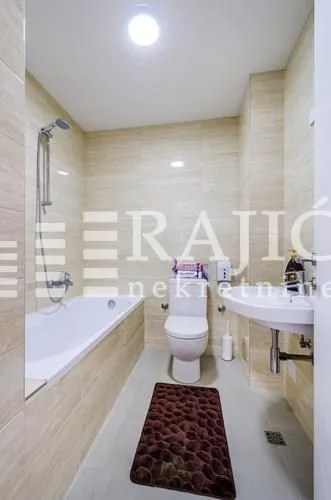 Small bathroom with a bathtub, sink, and toilet, tiled in light-colored tiles.