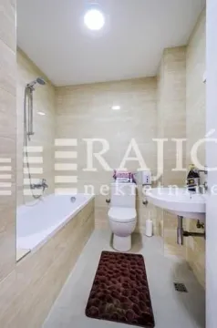 Small bathroom with a bathtub, sink, and toilet, tiled in light-colored tiles. - image 10