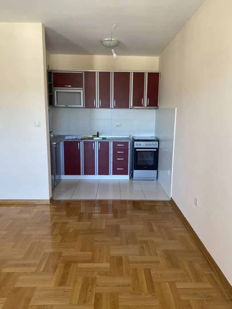 Jednostavna kuhinja sa crvenim elementima i drvenim podom u prednjem dijelu.