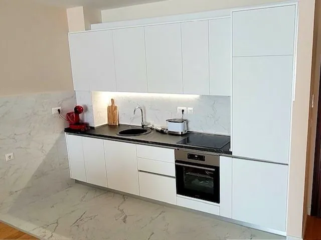 Modern white kitchen with a dark countertop and built-in appliances.