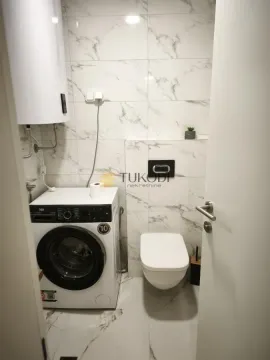 Smaller bathroom with white tiles, toilet, and washing machine. - image 6