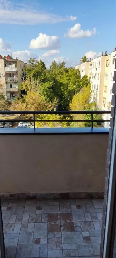 Pogled sa popločanog balkona na okolne zgrade i zelene površine.