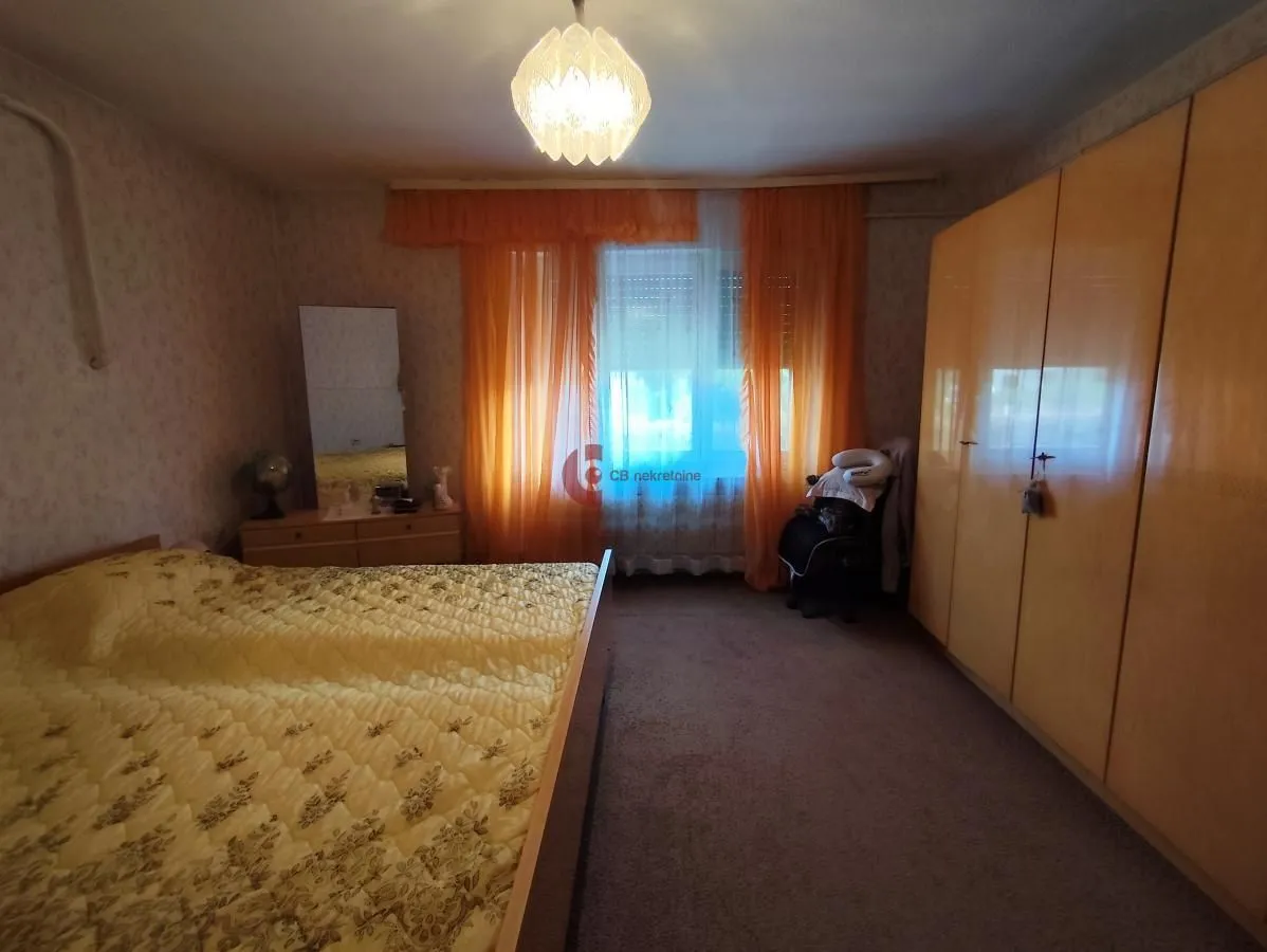 Furnished bedroom with a double bed, large wardrobe, and a window with orange curtains.