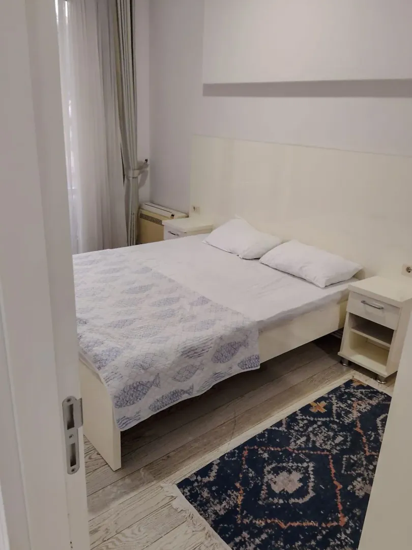 Spavaća soba sa bračnim krevetom, noćnim stočićima i prozorom sa zavjesama.