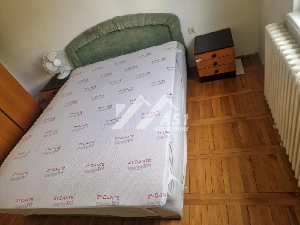 Furnished bedroom with a double bed, nightstand, and a fan.