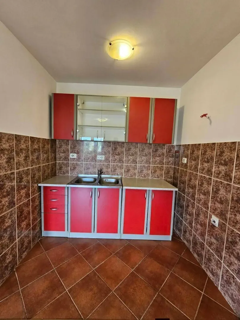Manja kuhinja sa crvenim elementima i braon pločicama na zidovima i podu.