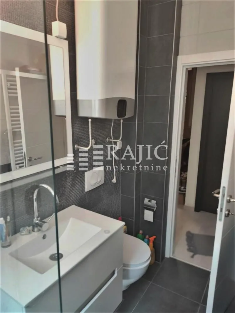 Modernly equipped bathroom with a washbasin, toilet bowl, and water heater.
