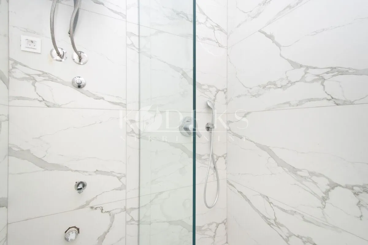 Modern shower with a glass partition in a marble bathroom.