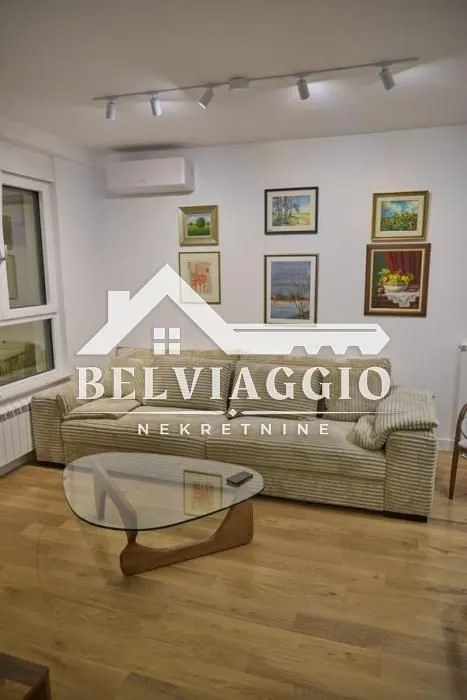 Living room with a large beige sofa, glass coffee table, and paintings on the wall.