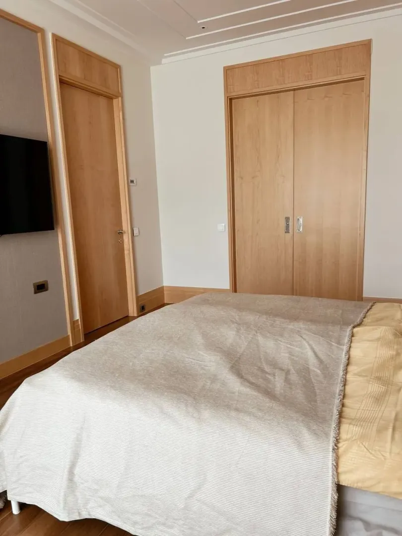 Spavaća soba sa bračnim krevetom, ugradnim ormarom i drvenim detaljima.