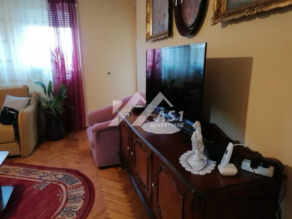 Dnevna soba sa garniturom, televizorom i drvenom komodom.