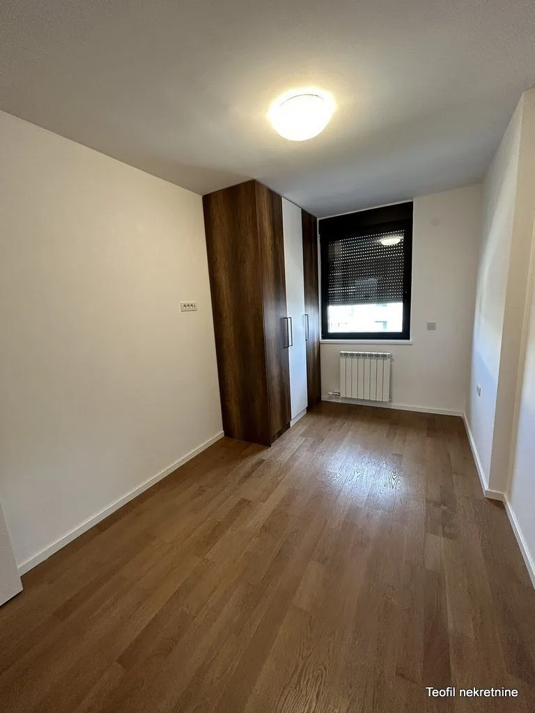 Prazna soba sa ugradnim ormanom, parketom i prozorom.