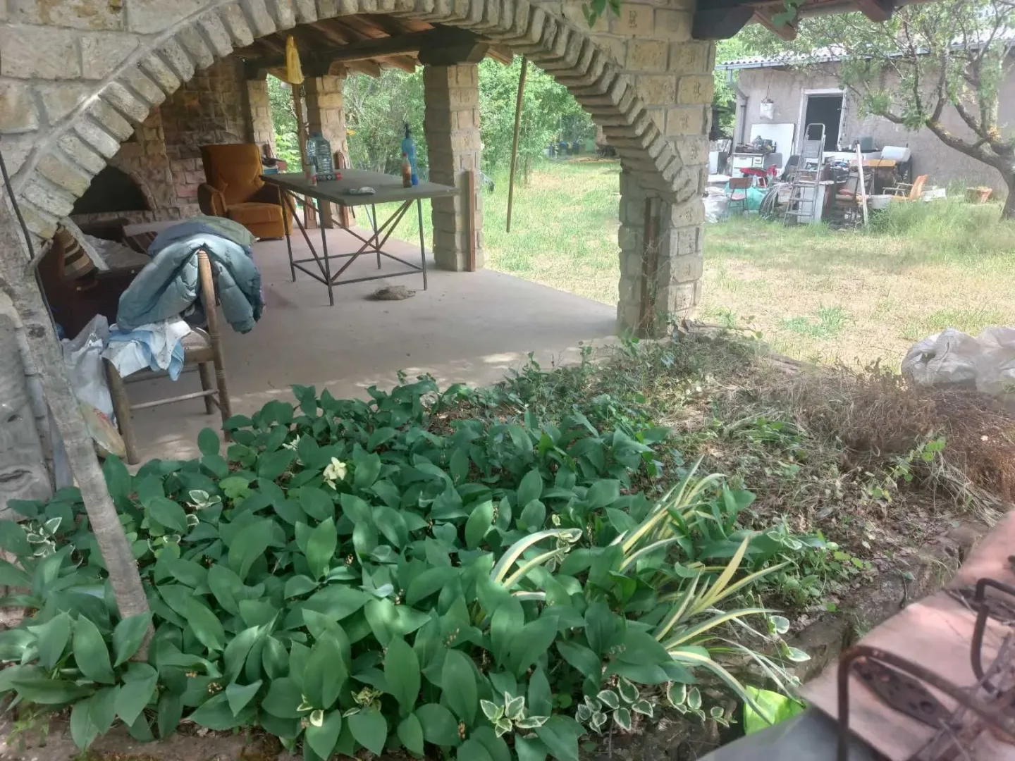 Natkrivena kamena terasa i dvorište kuće sa rastinjem.