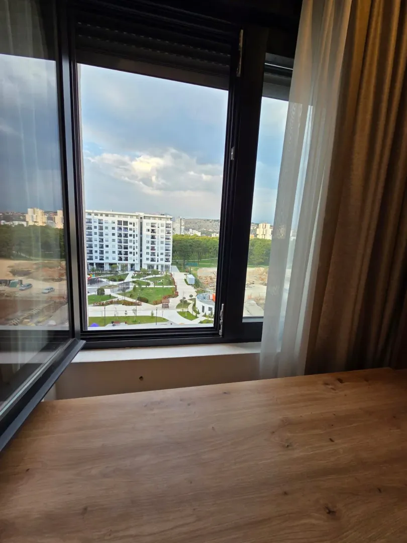 Pogled kroz prozor na okolne zgrade i zelenu površinu.
