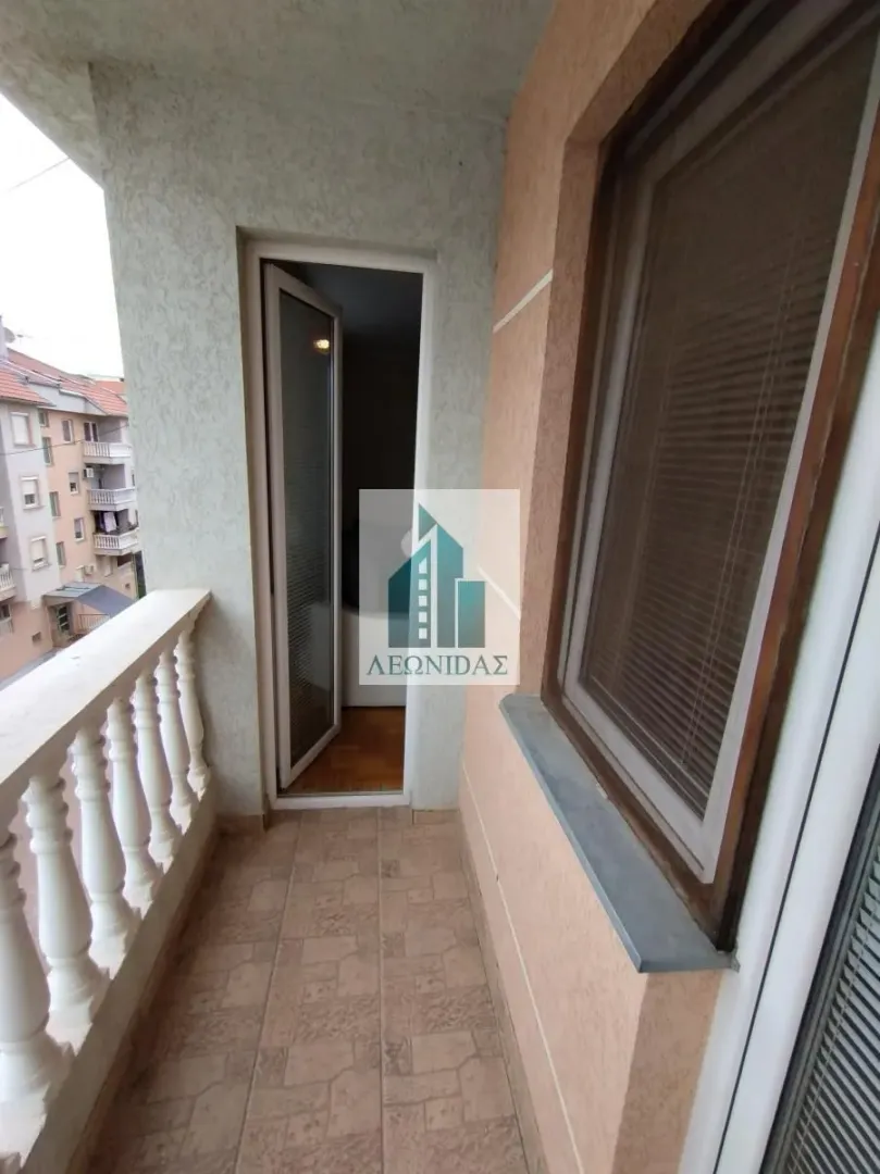 Small tiled balcony with a railing and a view of surrounding buildings.
