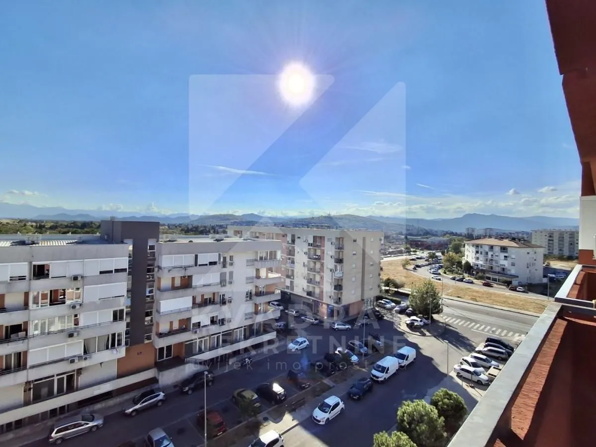 Pogled sa terase na okolne zgrade, parking i planine u daljini.