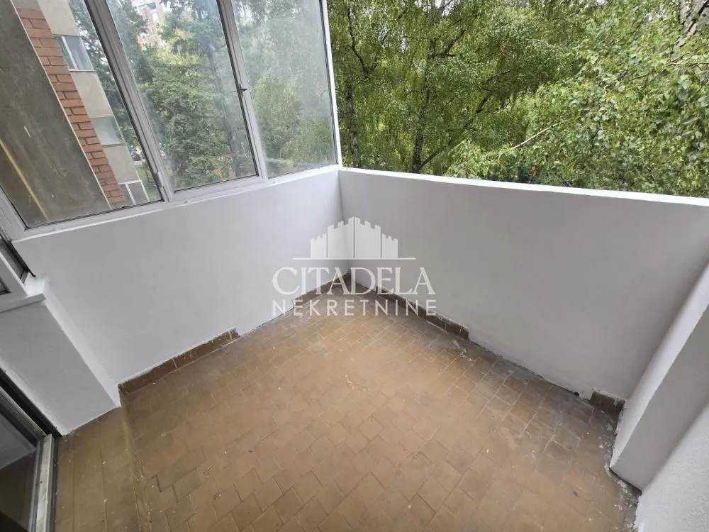 Zastakljeni balkon sa pogledom na zelenilo i okolne zgrade.