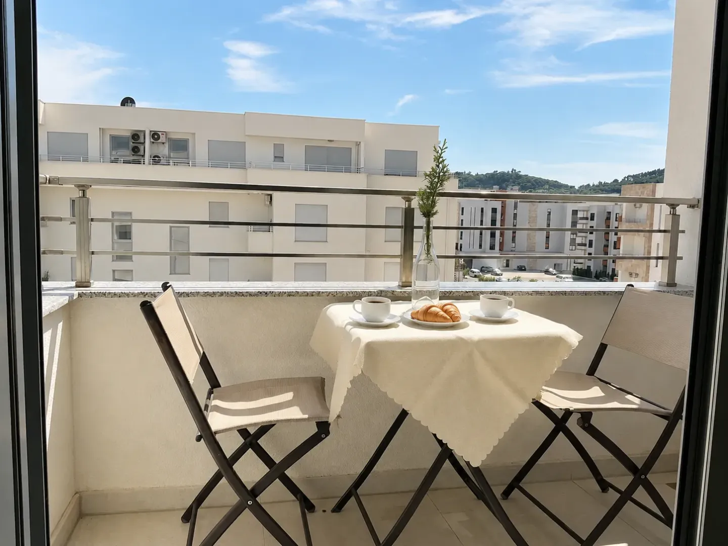 Namješten balkon sa stolom, stolicama i pogledom na okolne zgrade.