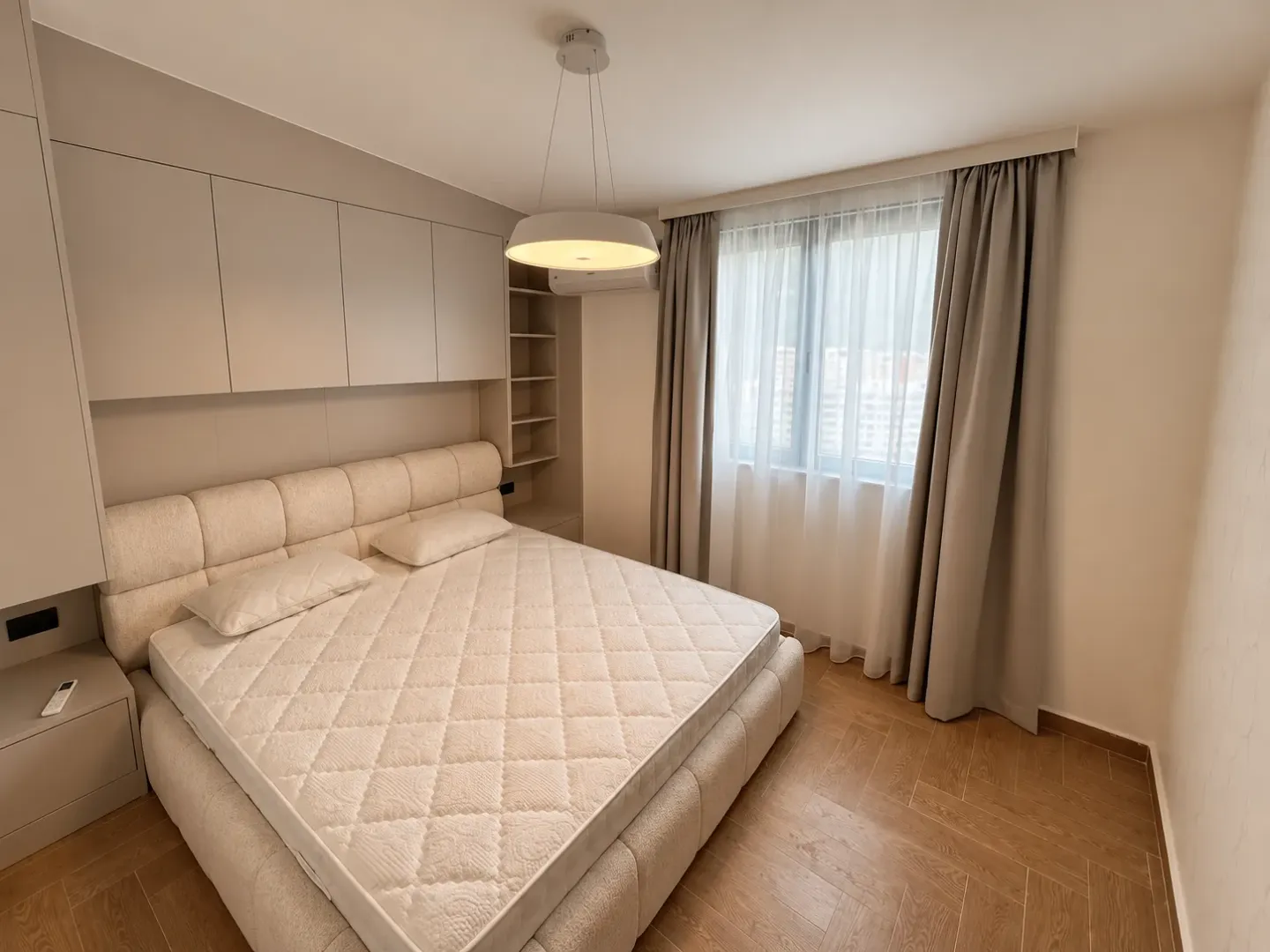 Moderna spavaća soba sa bračnim krevetom, ugradnim plakarima i prozorom sa zavjesama.