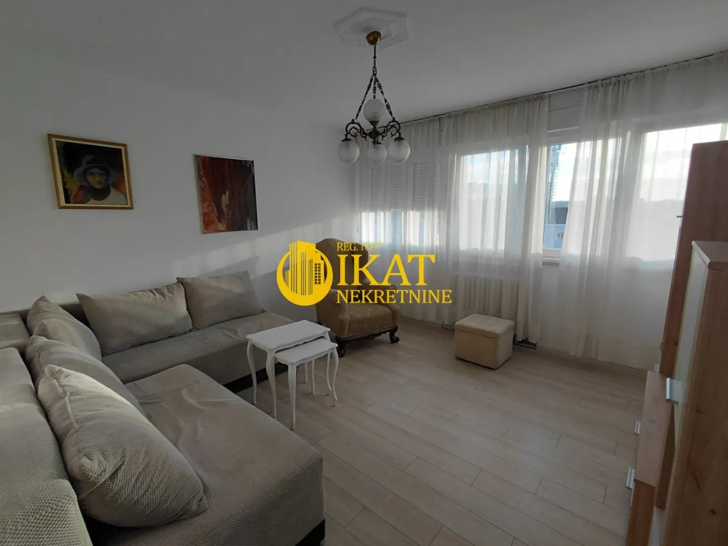 Living room with a sofa set, armchair, and windows with white curtains.