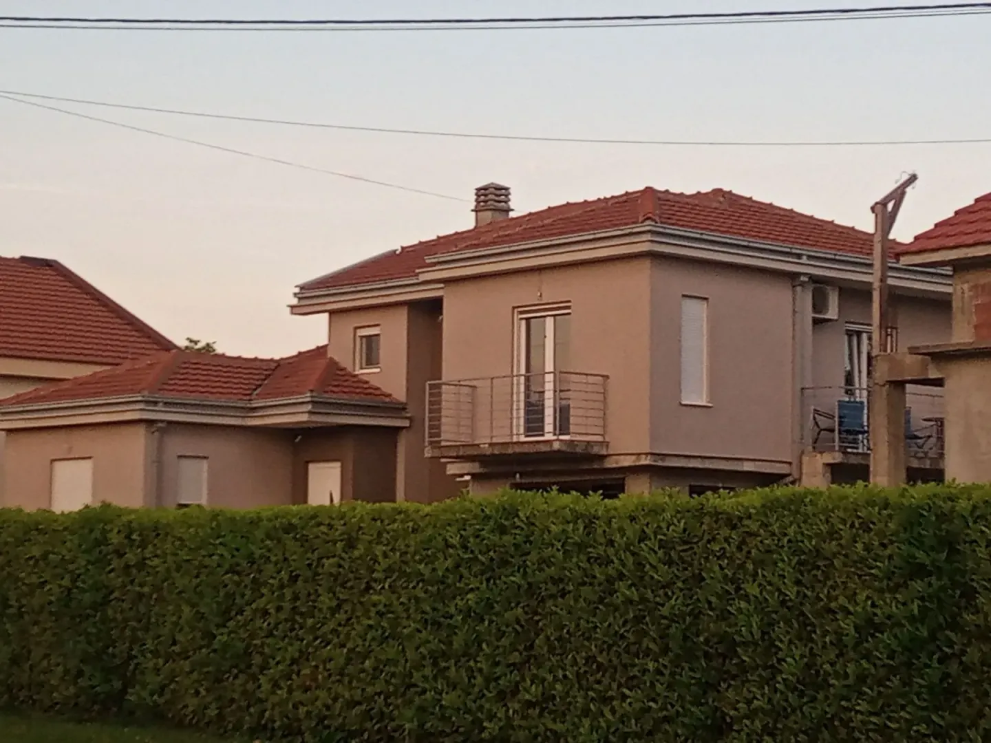 Exterior view of a two-story house behind a green hedge.