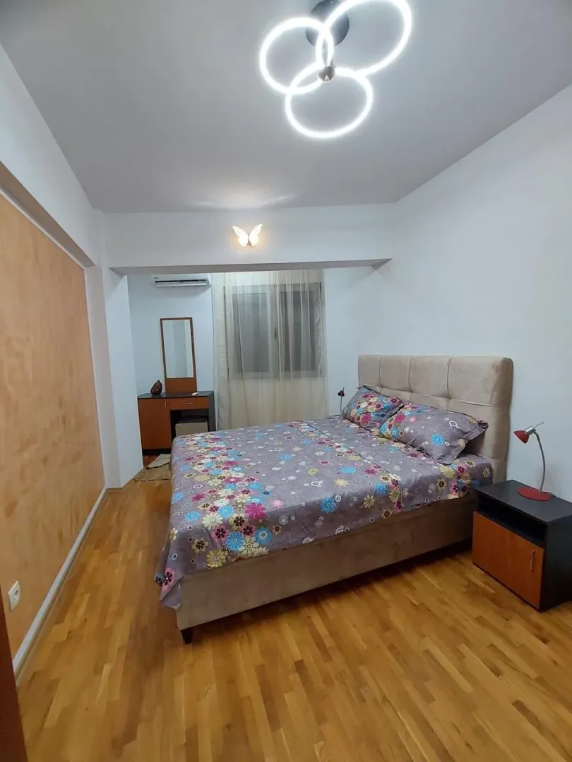 Furnished bedroom with a double bed, wooden flooring, and a dresser with a mirror.