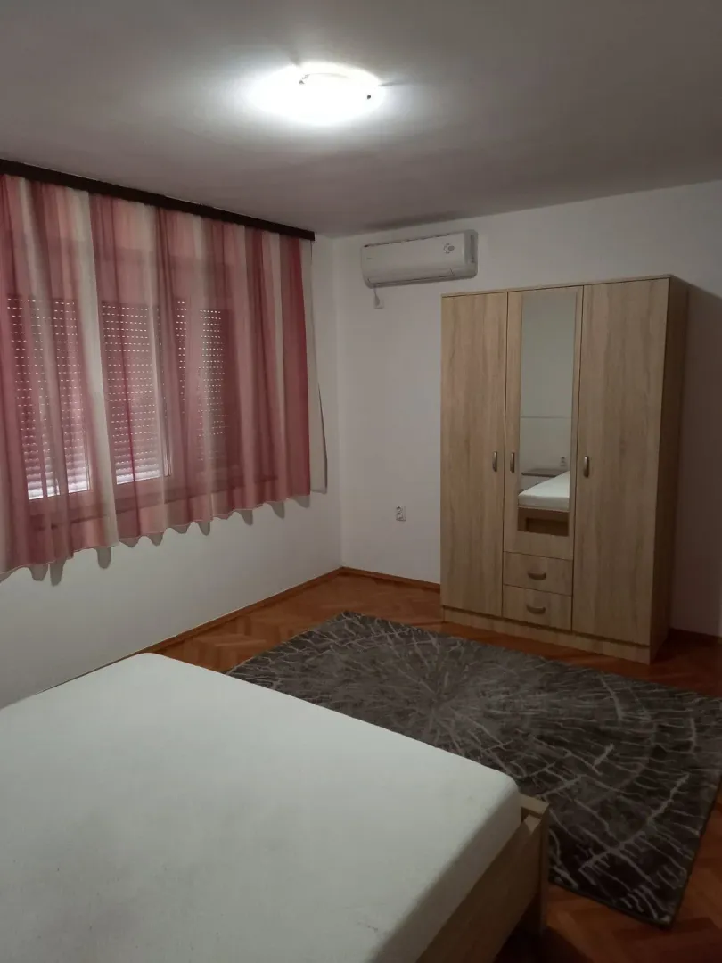 A bedroom with a wooden wardrobe, bed, and a rug.