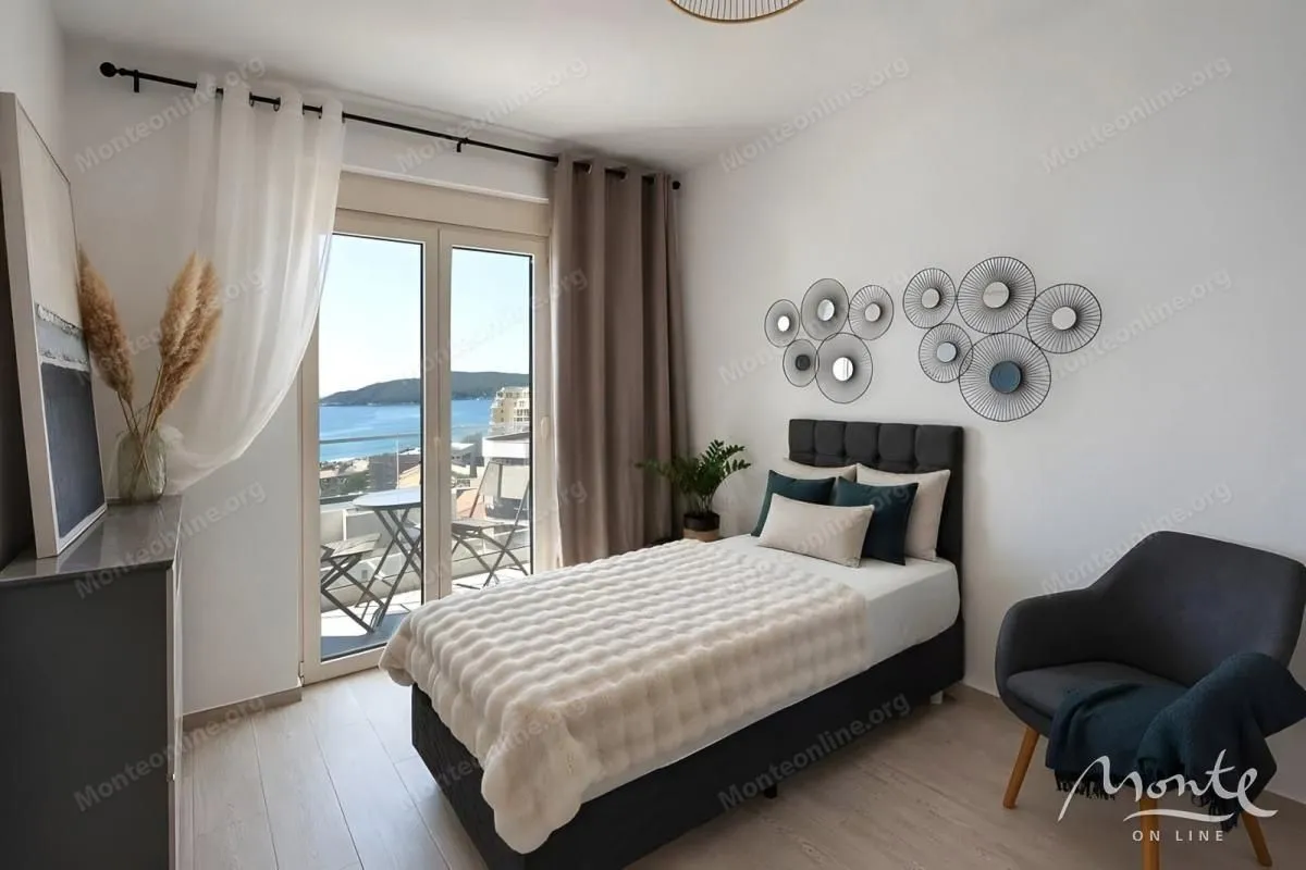 Namještena spavaća soba sa bračnim krevetom, foteljom i izlazom na balkon sa pogledom na more.