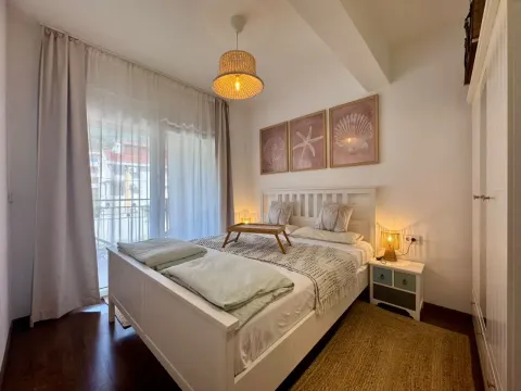 A furnished bedroom with a white bed and balcony doors. - image 14